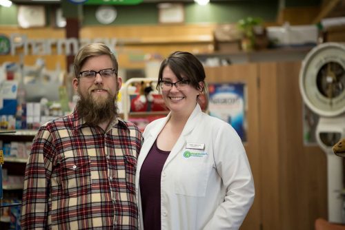 an image of a man in a flannel shirt standing next to a woman in a white lab coat inside the Corner Drug Co store