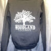 The back of a black hooded pullover sweatshirt with a white Woodland logo featuring a silhouette of a large tree