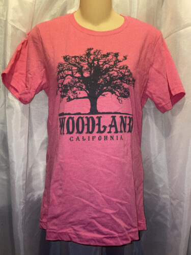 A salmon colored t-shirt with a large black Woodland logo featuring a silhouette of a tree
