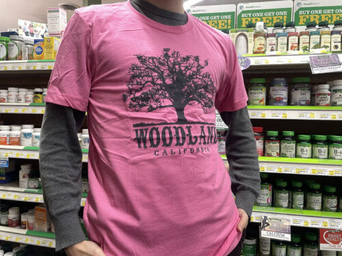A person wearing a salmon colored t-shirt with a large black Woodland logo featuring a silhouette of a tree